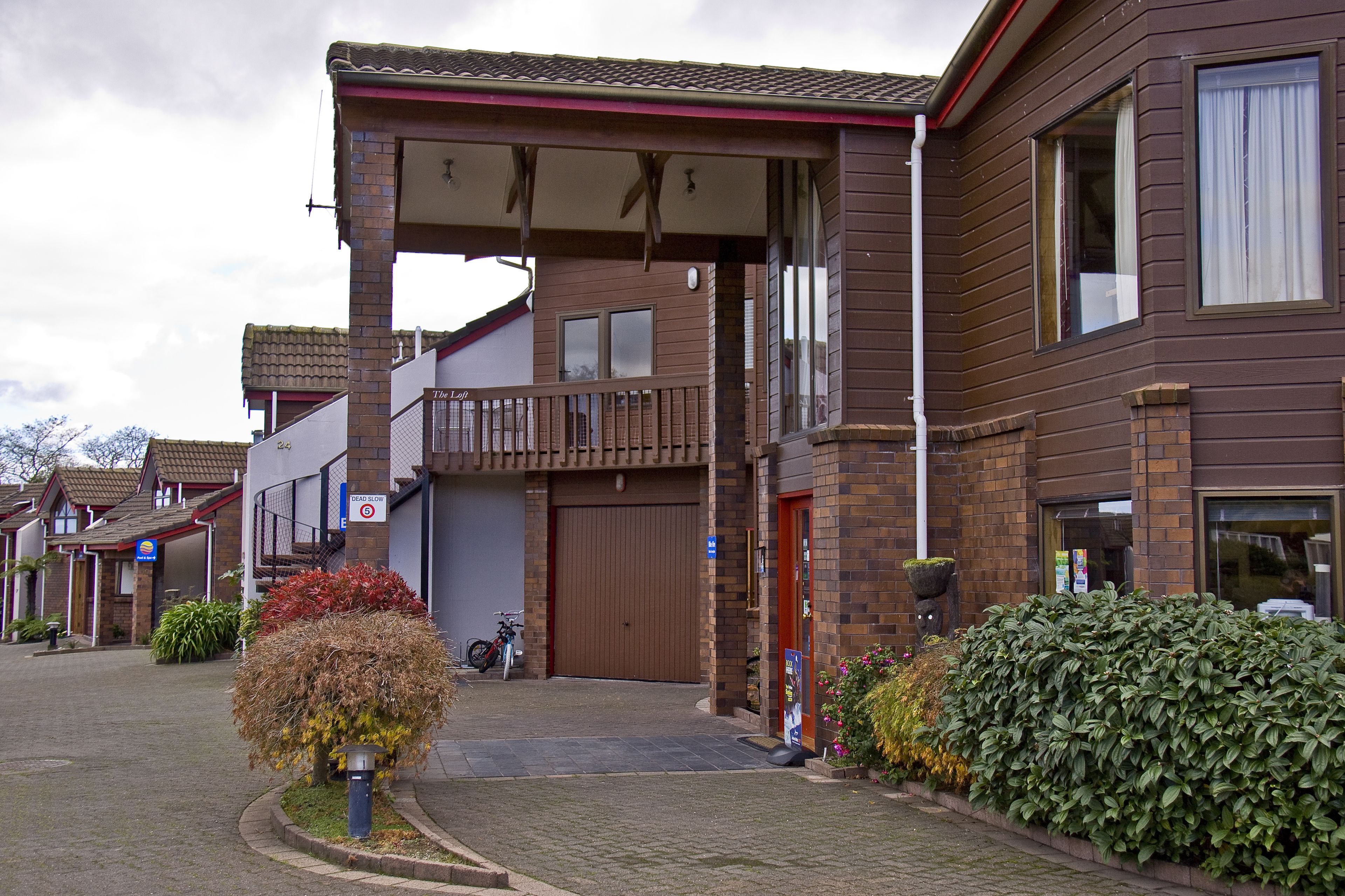 Een gebouw met twee verdiepingen, een overdekte ingang, een zichtbare garagepoort en een klein balkon.