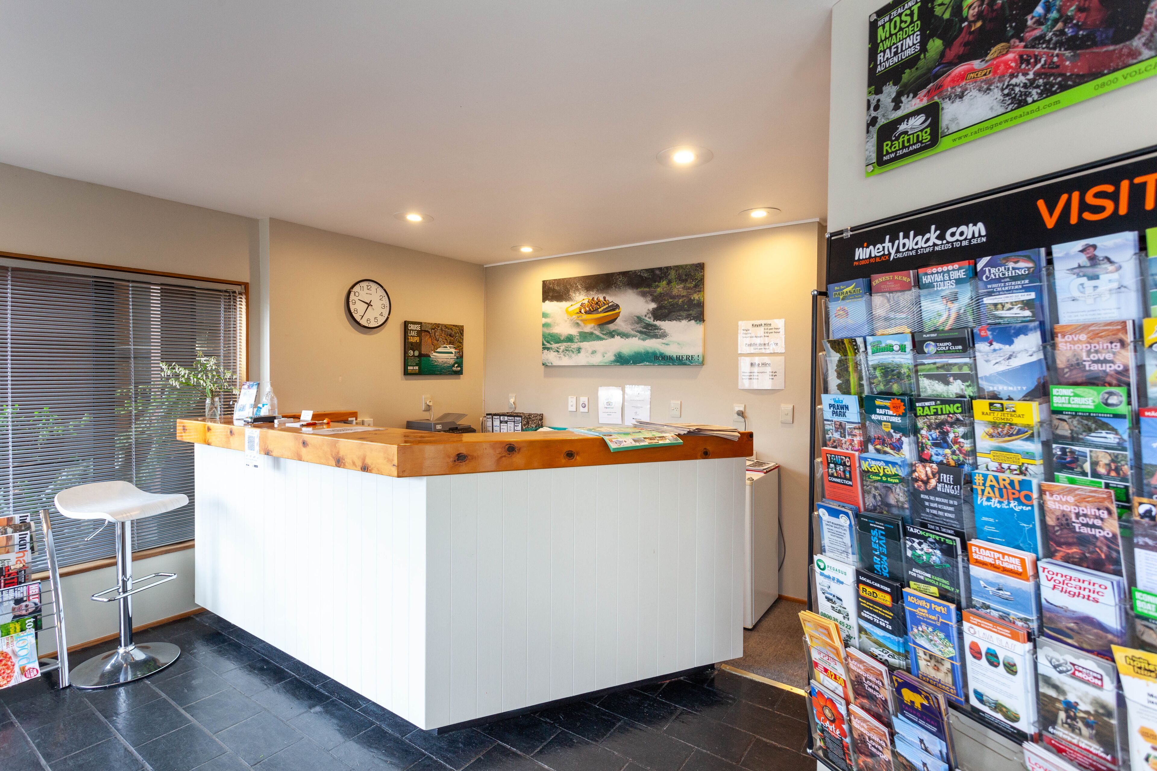 A reception desk with a wooden top and white base, a clock on the wall, and a bulletin board with various travel brochures.