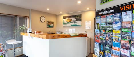 A reception desk with a wooden top and white base, a clock on the wall, and a bulletin board with various travel brochures.