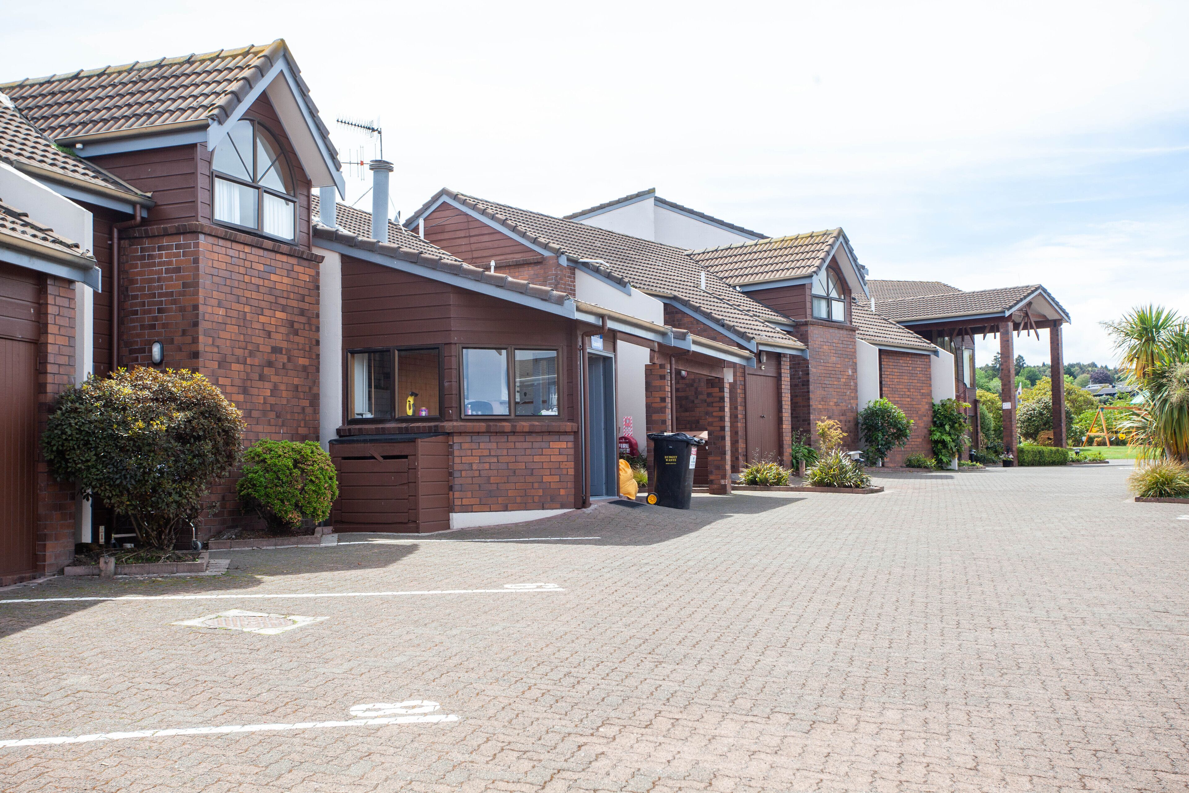 A row of brick houses with tiled roofs and a paved driveway.