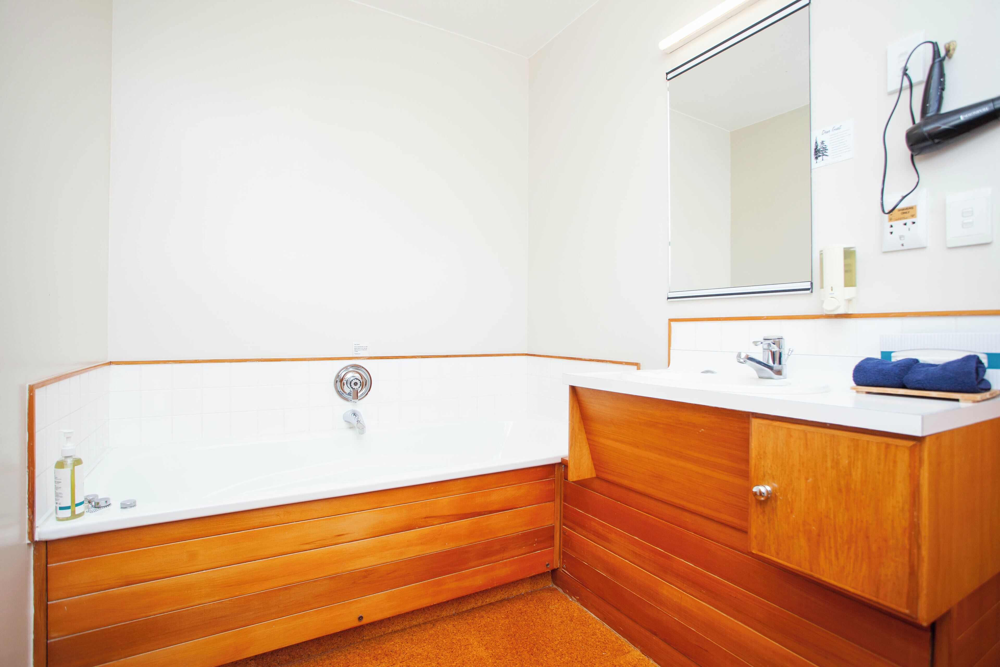 Un baño con tocador de madera, bañera blanca y espejo sobre el lavabo.