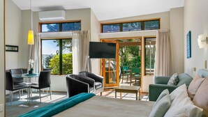 A hotel room with a bed, a desk with a chair, a TV, and a balcony with a table and chairs. - Cascades Lakefront Motel (Taupo)