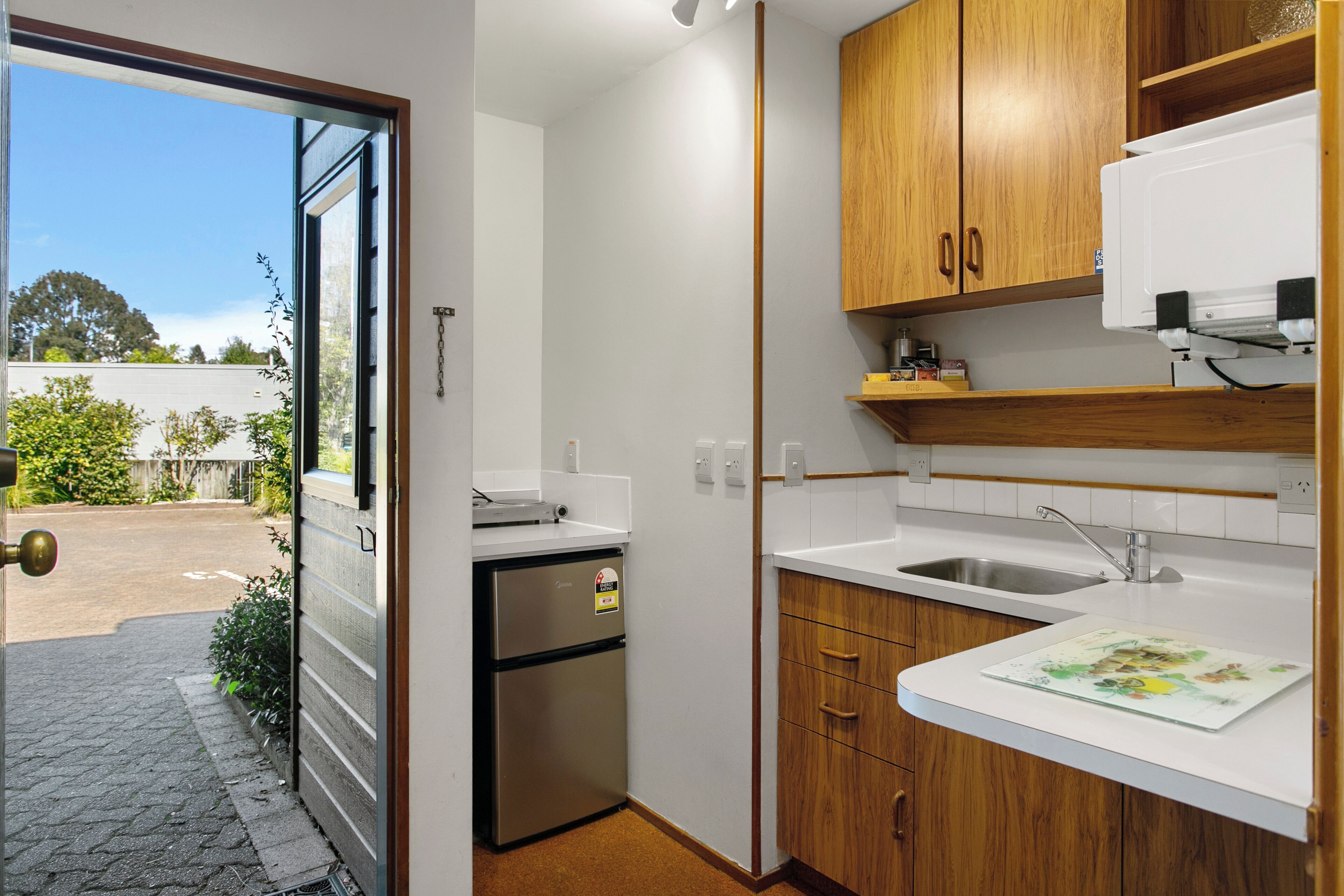A compact kitchen with wooden cabinets, a built-in microwave, and a stainless steel refrigerator.