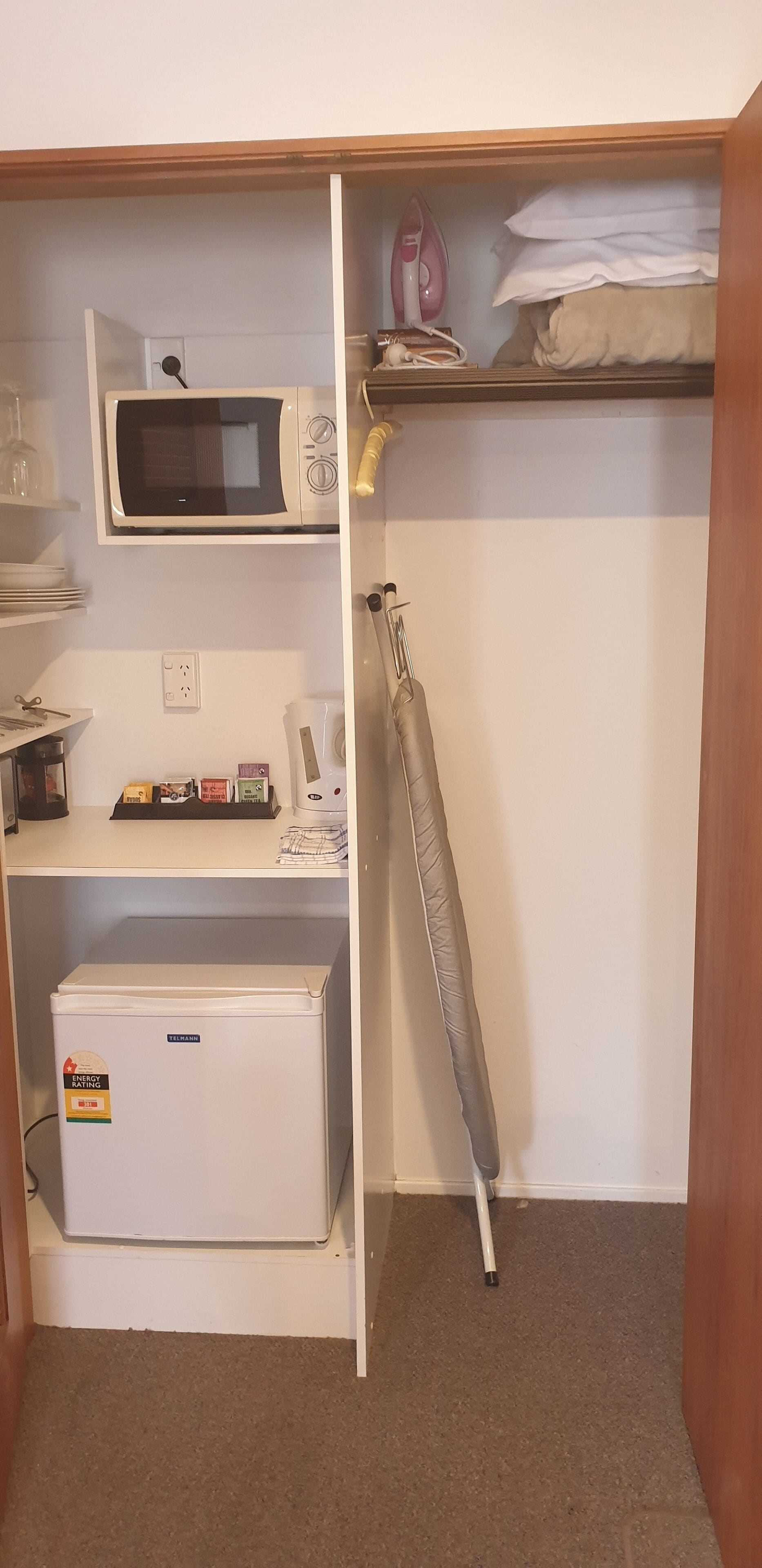 Eine kompakte Küchenzeile mit einer Mikrowelle, einem kleinen Kühlschrank und einem Regal mit gefalteten Handtüchern.