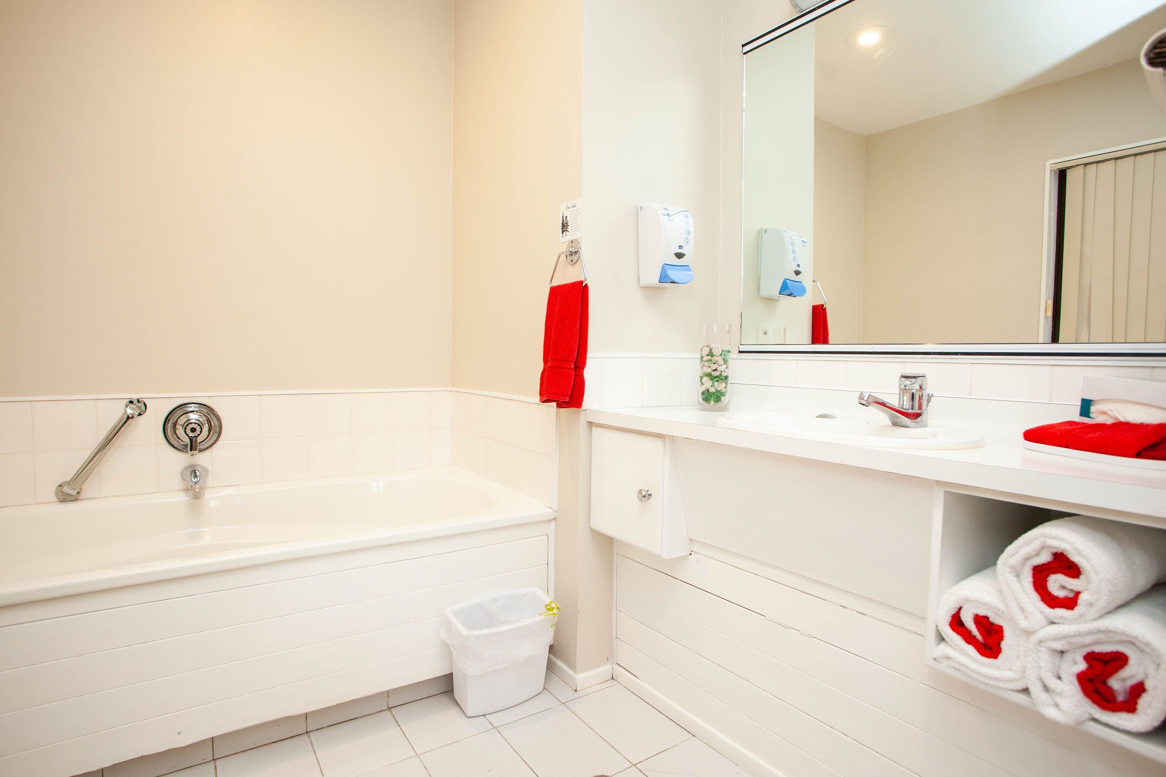 A modern bathroom with a white bathtub, a sink, and a mirror. There are towels and toiletries visible.