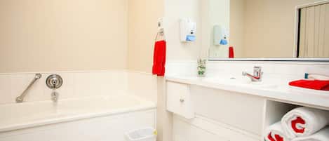 A modern bathroom with a white bathtub, a sink, and a mirror. There are towels and toiletries visible.