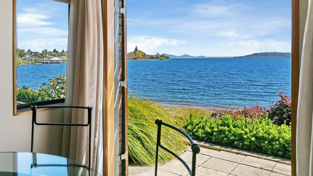 A room with a glass table and chairs, a view of a lake, and a distant island. - Cascades Lakefront Motel (Taupo)