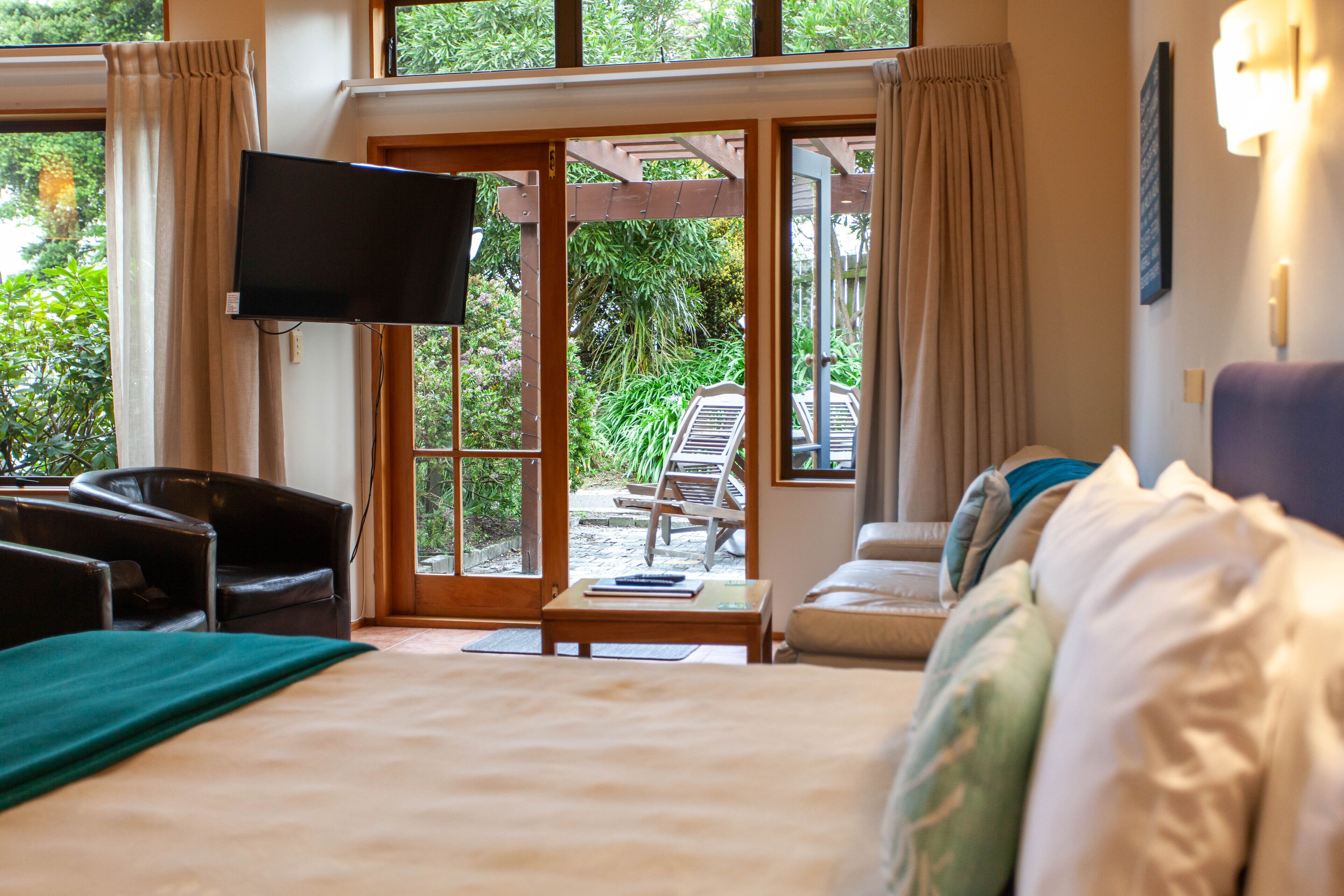 Une chambre d’hôtel avec un lit, un téléviseur fixé au mur, un canapé et une vue sur le jardin, visible à travers la porte vitrée.