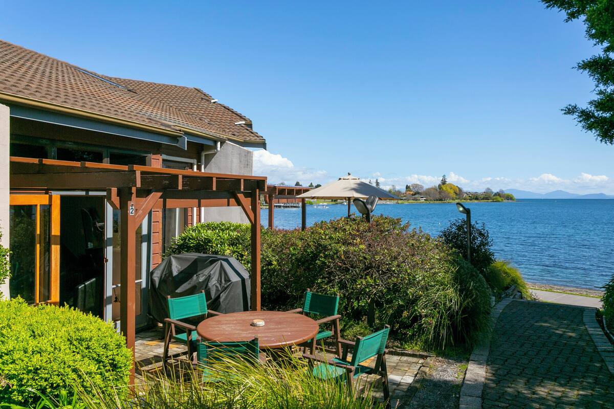 Une terrasse avec une table et des chaises, un barbecue couvert et une vue sur le lac.
