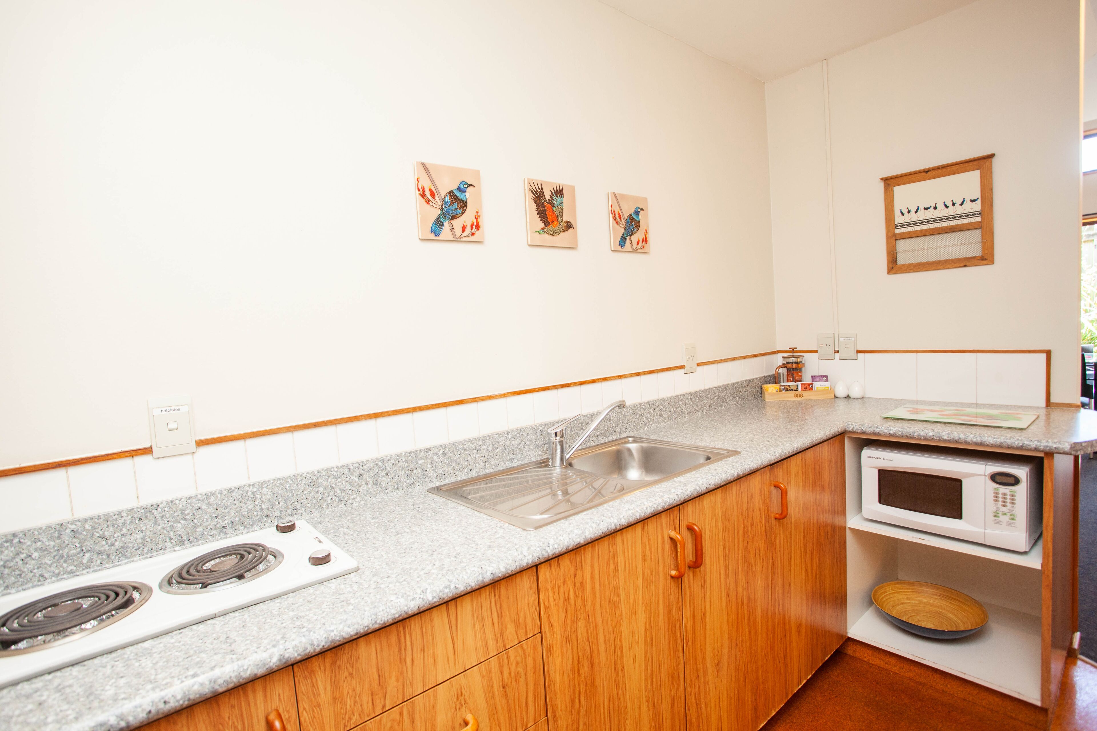 A kitchen with granite countertops, wooden cabinets, a stainless steel sink, a microwave, and a stove. There are three wall-mounted bird paintings.