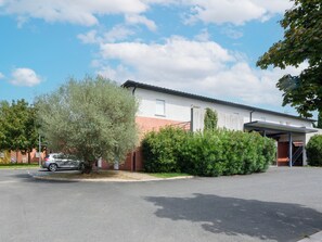 Un bâtiment à deux étages avec un garage, un espace de stationnement couvert et un arbre devant.