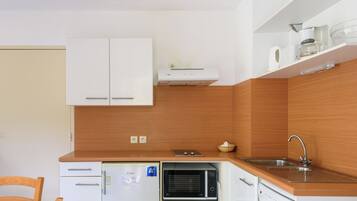 Cocina compacta con armarios blancos, microondas, horno empotrado, pileta y mesa de comedor de madera.