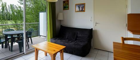 A room with a sofa, a wooden table, a chair, and a balcony with chairs.