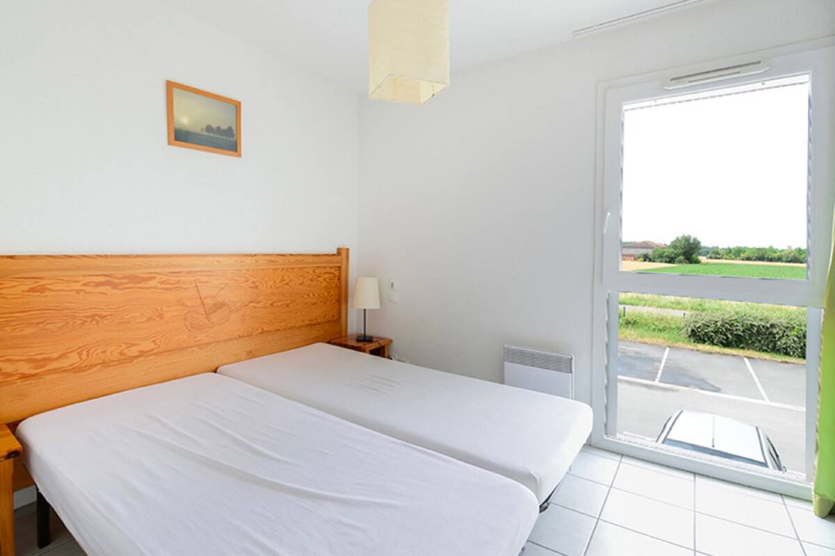 Een hotelkamer met een houten hoofdeinde, een bed met witte lakens, een nachtkastje met een lamp en uitzicht op een groen landschap door een glazen schuifdeur.
