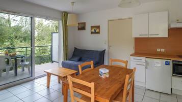 Un espacio habitable compacto con comedor, sofá, cocina y balcón con vistas a zonas verdes.