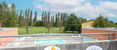 A rooftop terrace with a table set for breakfast, overlooking a swimming pool and a grassy area with trees.