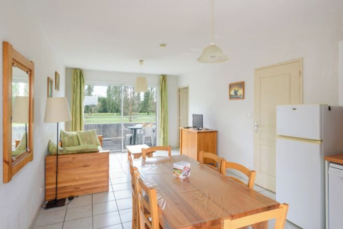 A compact kitchen with a dining table, chairs, a refrigerator, and a sofa with a table.
