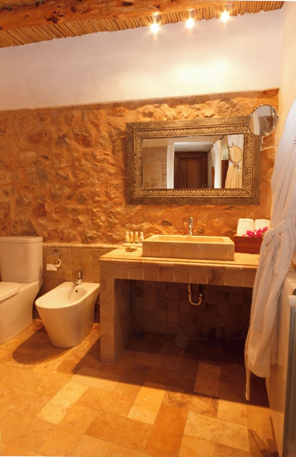 A bathroom with a stone wall, a sink with a mirror, a bidet, and a bathtub. - Can Pardal (Sant Joan de Labritja)