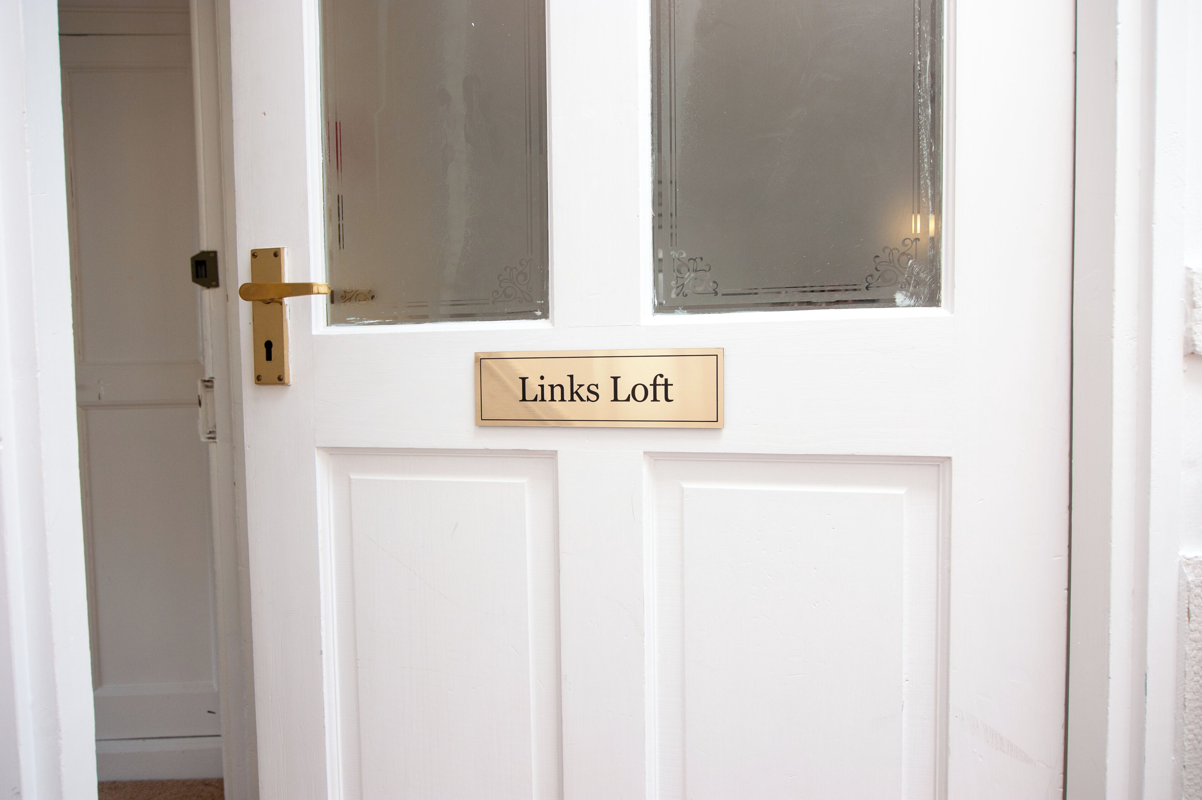 A white door with a brass handle and a nameplate that reads "Links Loft".