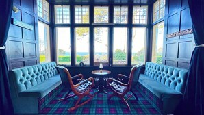 A room with two blue upholstered sofas facing a large window with multiple panes, a small round table, and a wooden rocking chair. - Invernairne Guest House (Nairn)