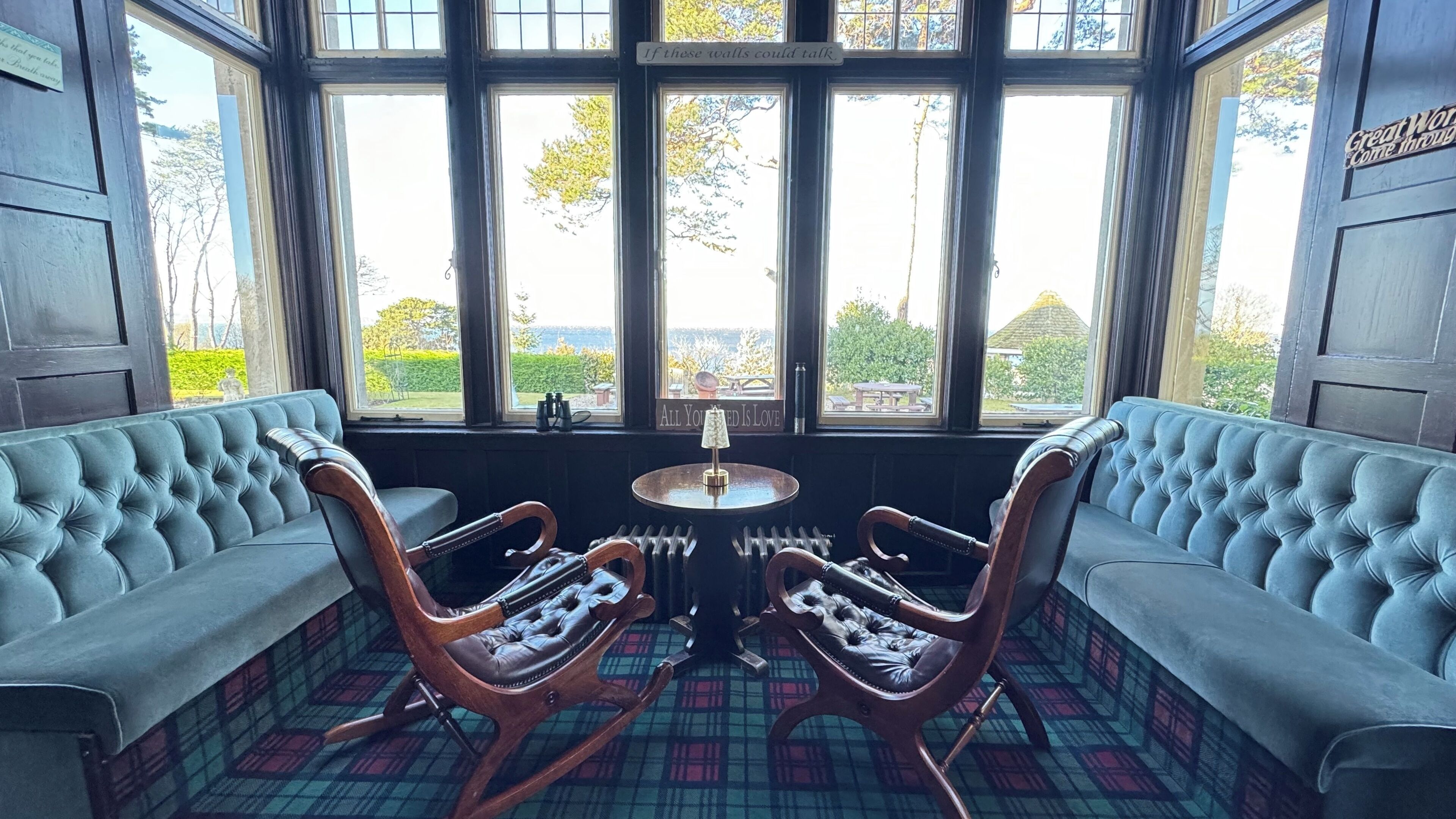 A room with a large bay window, two upholstered sofas, a small table with a lamp, and a plaid-patterned floor.