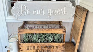 Une pancarte en bois rustique portant l’inscription « Soyez nos invités » au-dessus d’une caisse en bois remplie de plants de lavande.