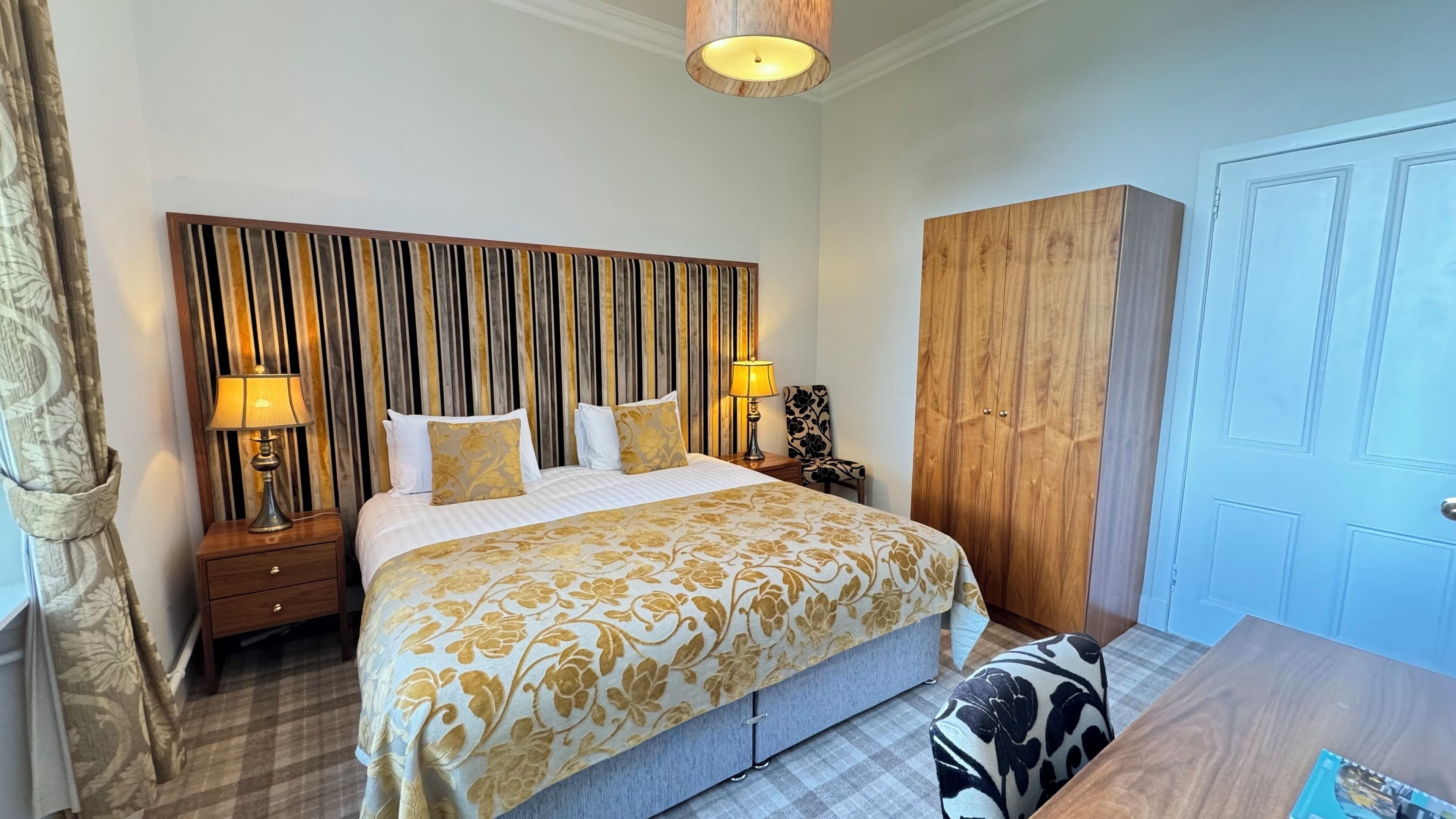 A hotel room with a large bed, two bedside tables with lamps, a wardrobe, and a checkered floor.