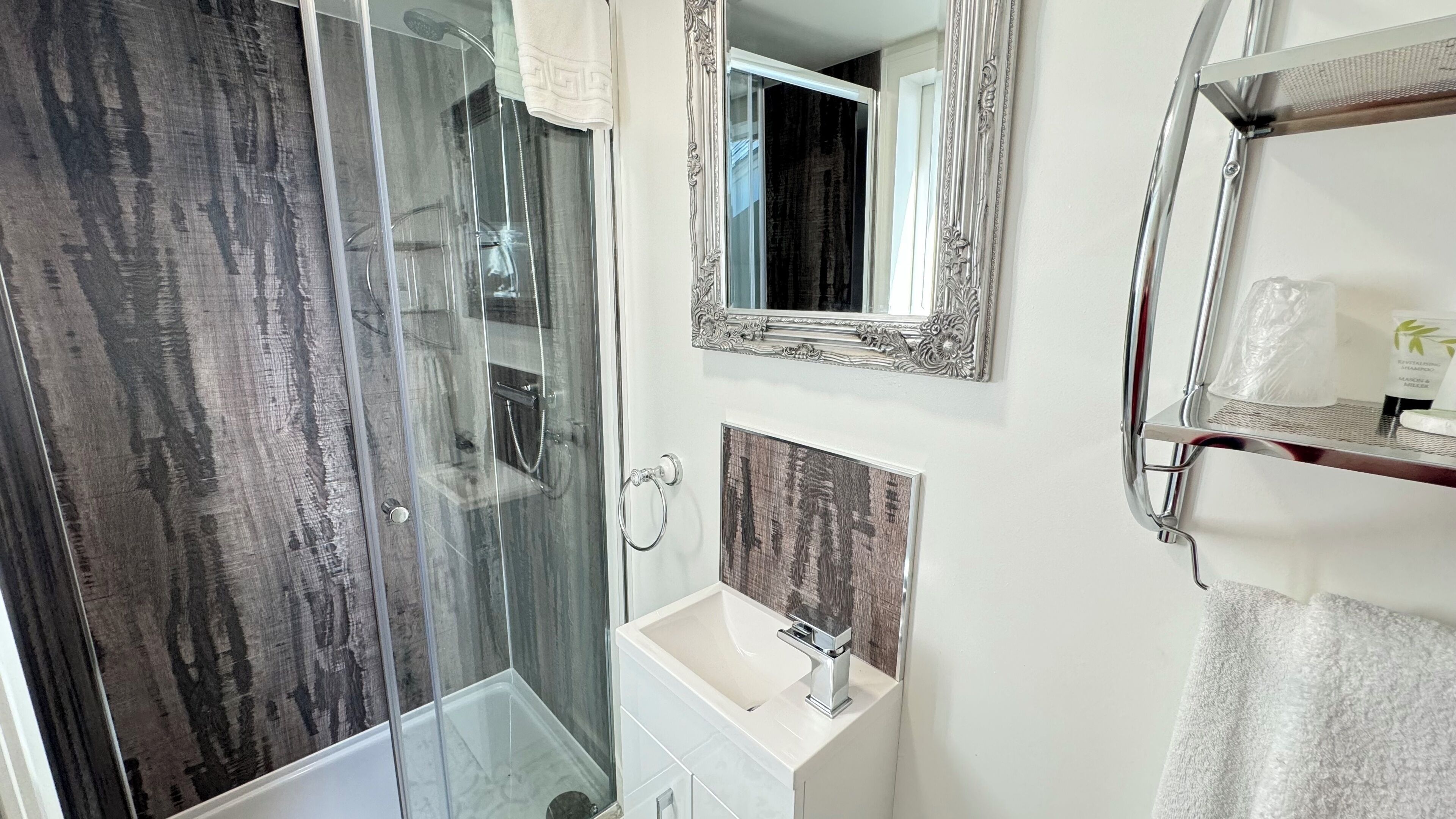 A modern bathroom with a glass shower enclosure, a vanity with a mirror, and a towel rack.