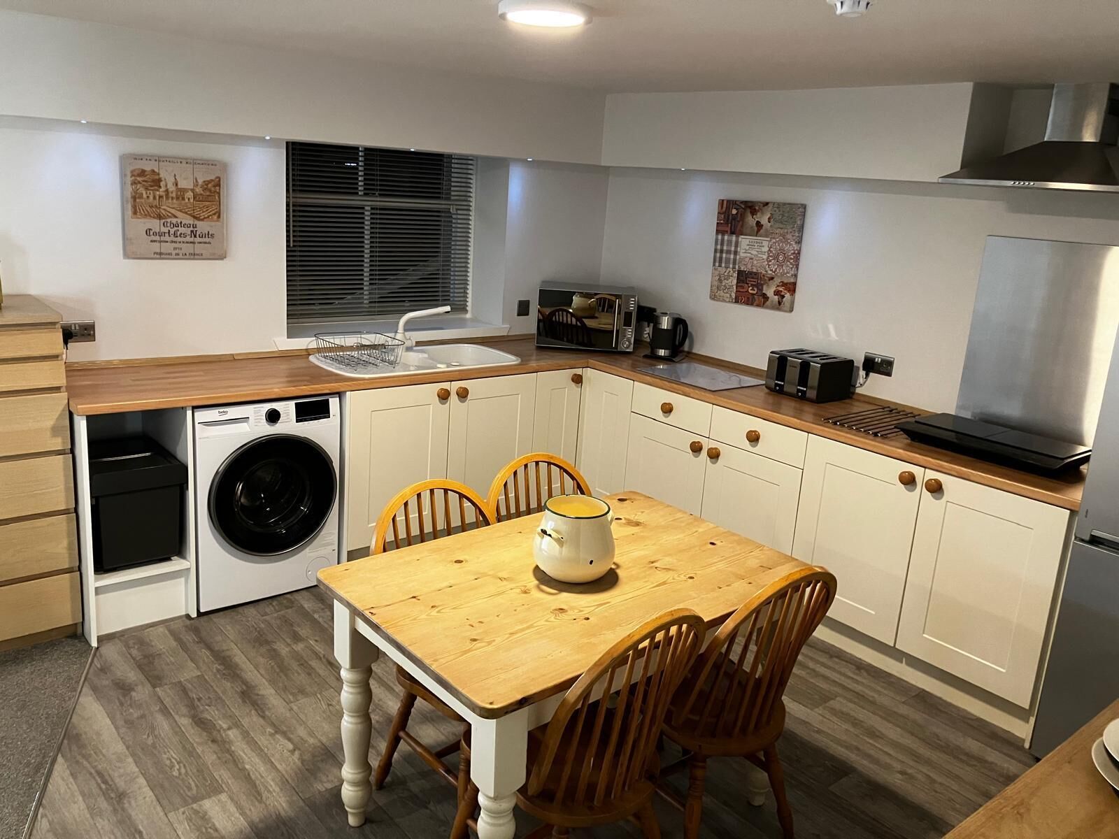 A compact kitchen with a washing machine, a sink, a dining table with chairs, and a stove.
