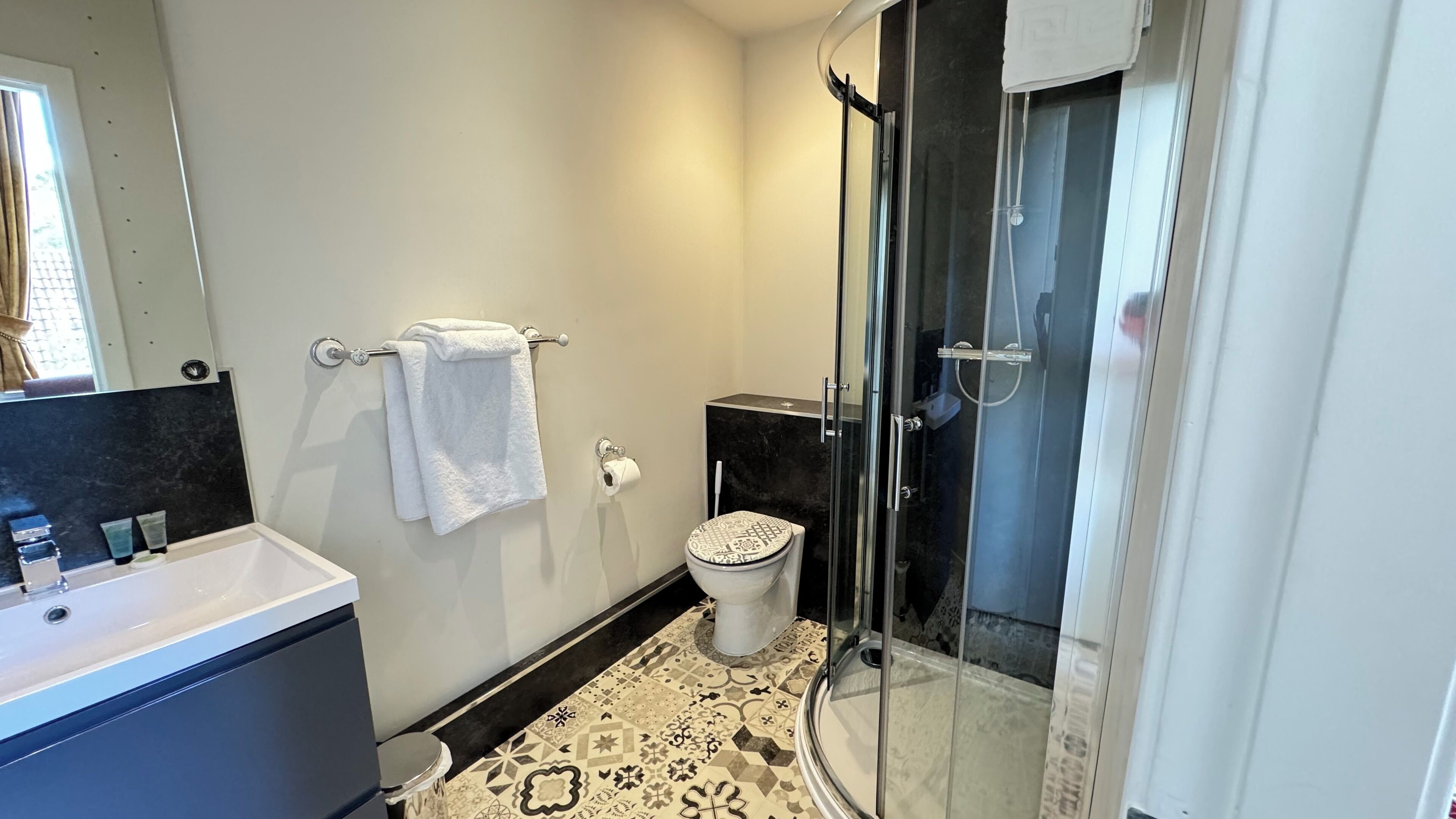 Un baño moderno con cabina de ducha de vidrio, inodoro blanco y lavamanos con encimera negra.