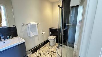 Un baño moderno con cabina de ducha de vidrio, inodoro blanco y lavamanos con encimera negra.