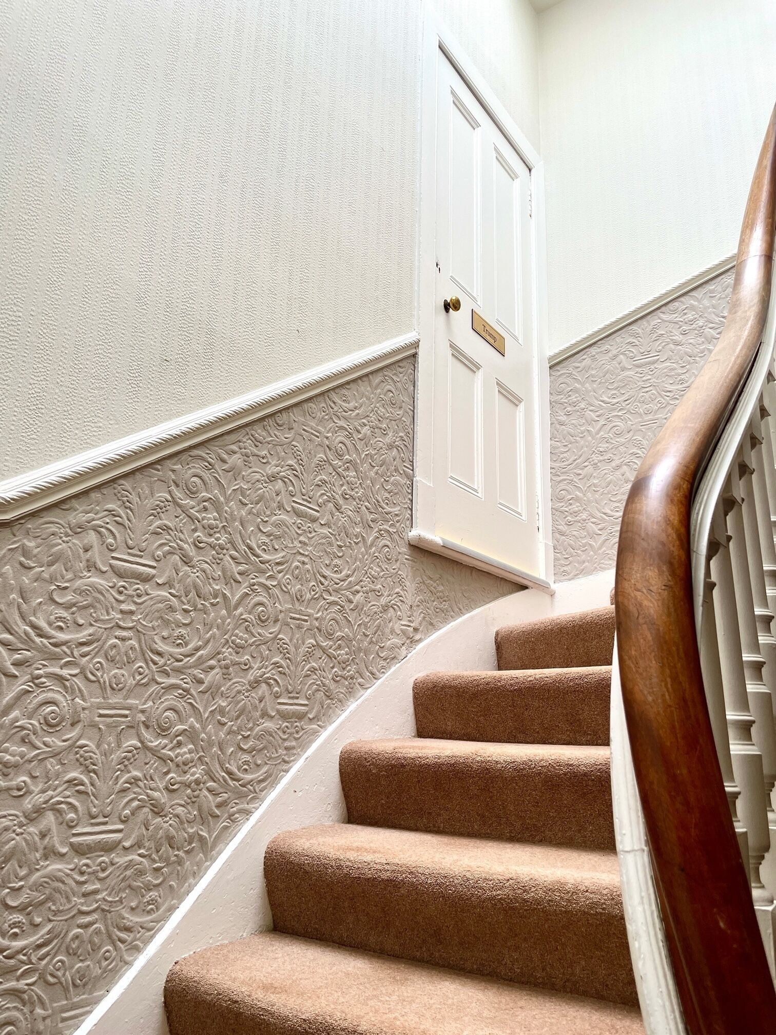 A staircase with a wooden handrail, beige carpeted steps, and a white door with a brass handle.