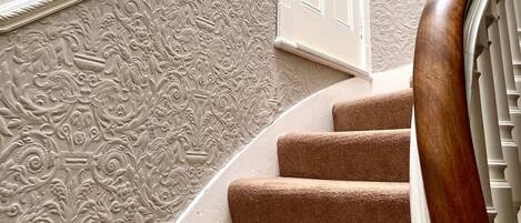 A staircase with a wooden handrail, beige carpeted steps, and a white door with a brass handle.