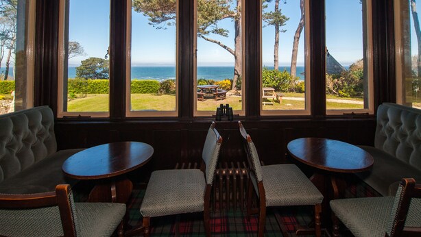 A room with large windows offering a view of the sea and a lawn with outdoor seating. - Invernairne Guest House (Nairn)