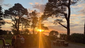 A group of people gathered outdoors at sunset, with a view of the sun setting behind trees. - Invernairne Guest House (Nairn)