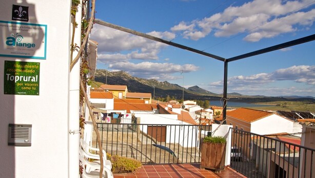 Un balcón con vistas a un pueblo y montañas. Hay carteles que dicen 'alange' y 'Toprural' en la pared.
