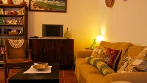 Una sala de estar acogedora con un sofá, una mesa de centro, una estantería, un cuadro y un televisor.