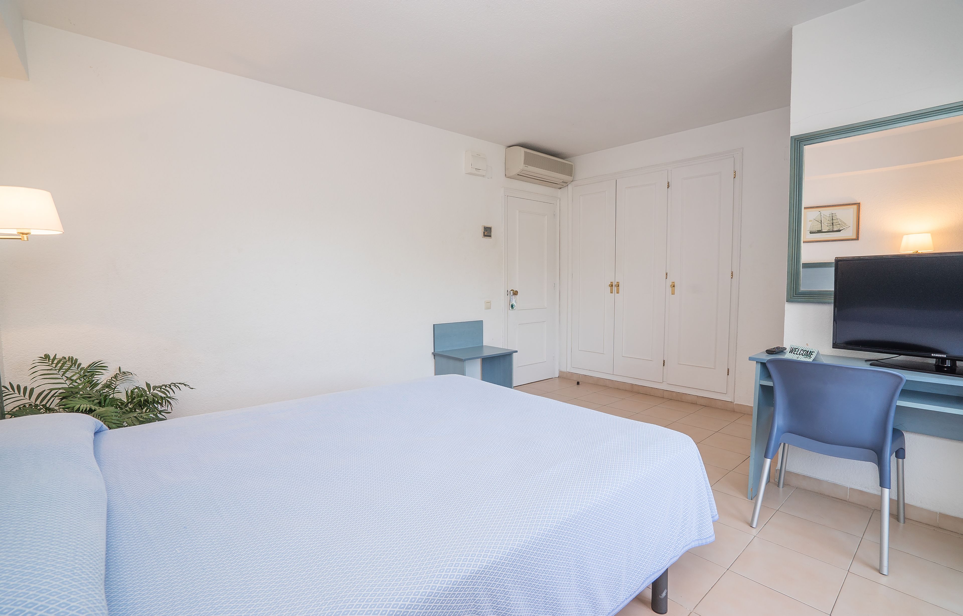 Quarto de hotel com uma cama, uma escrivaninha com cadeira, televisão e um guarda-roupa.