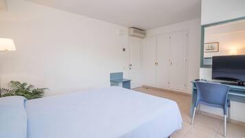 Quarto de hotel com uma cama, uma escrivaninha com cadeira, televisão e um guarda-roupa.