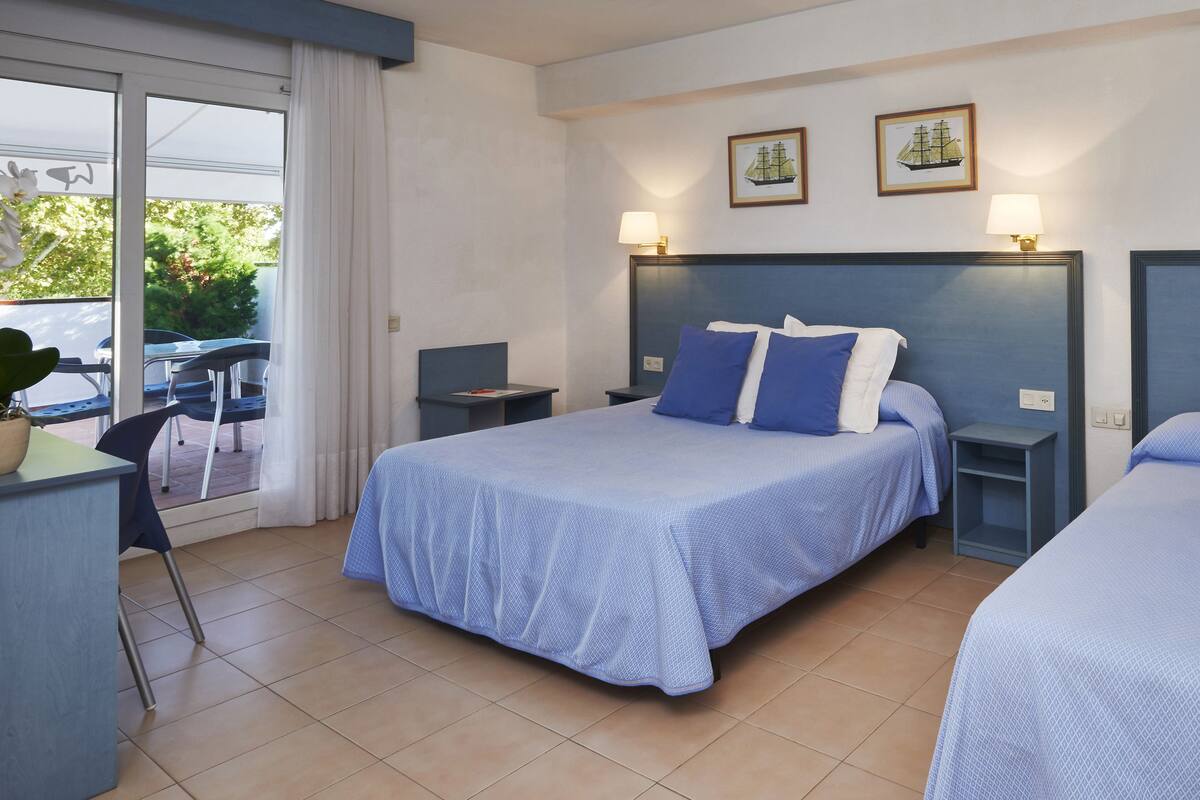 A hotel room with two beds, a desk, and a chair. There are two bedside tables with lamps.