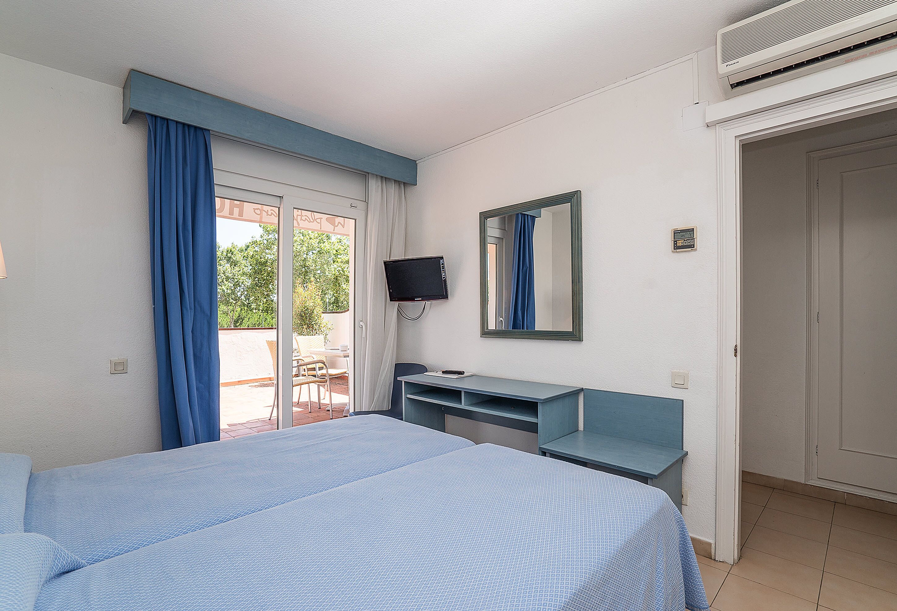 Ein Hotelzimmer mit einem Bett, einem Schreibtisch, einem Fernseher und einer Glastür zum Balkon.