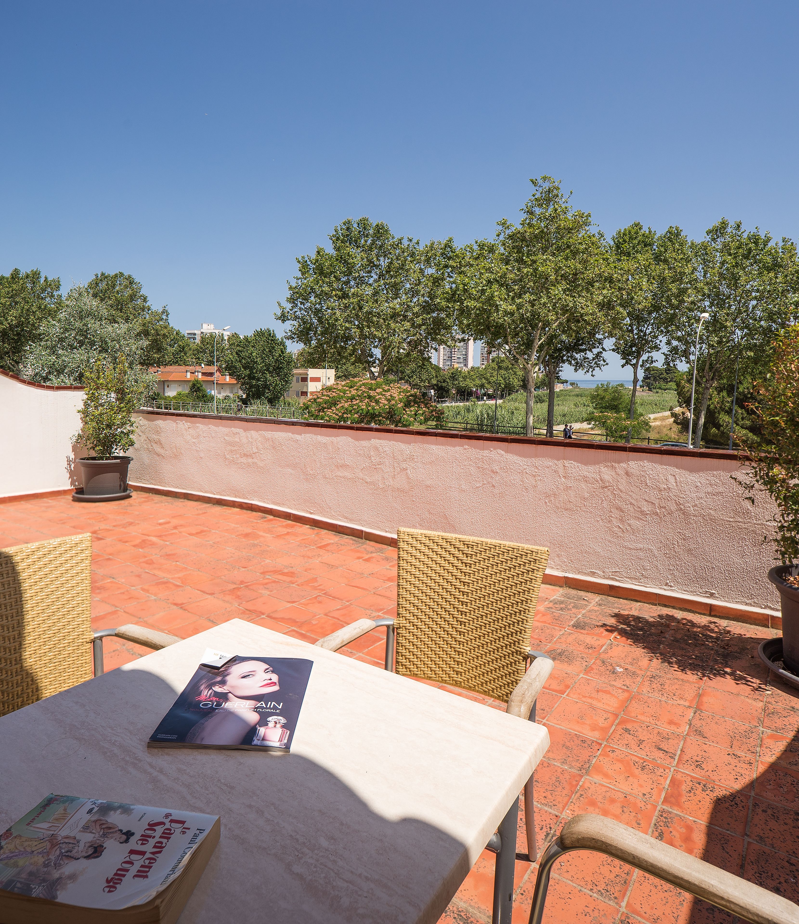 Un patio al aire libre con baldosas de terracota, sillas de mimbre y una mesa con una revista.