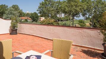 Un patio al aire libre con baldosas de terracota, sillas de mimbre y una mesa con una revista.