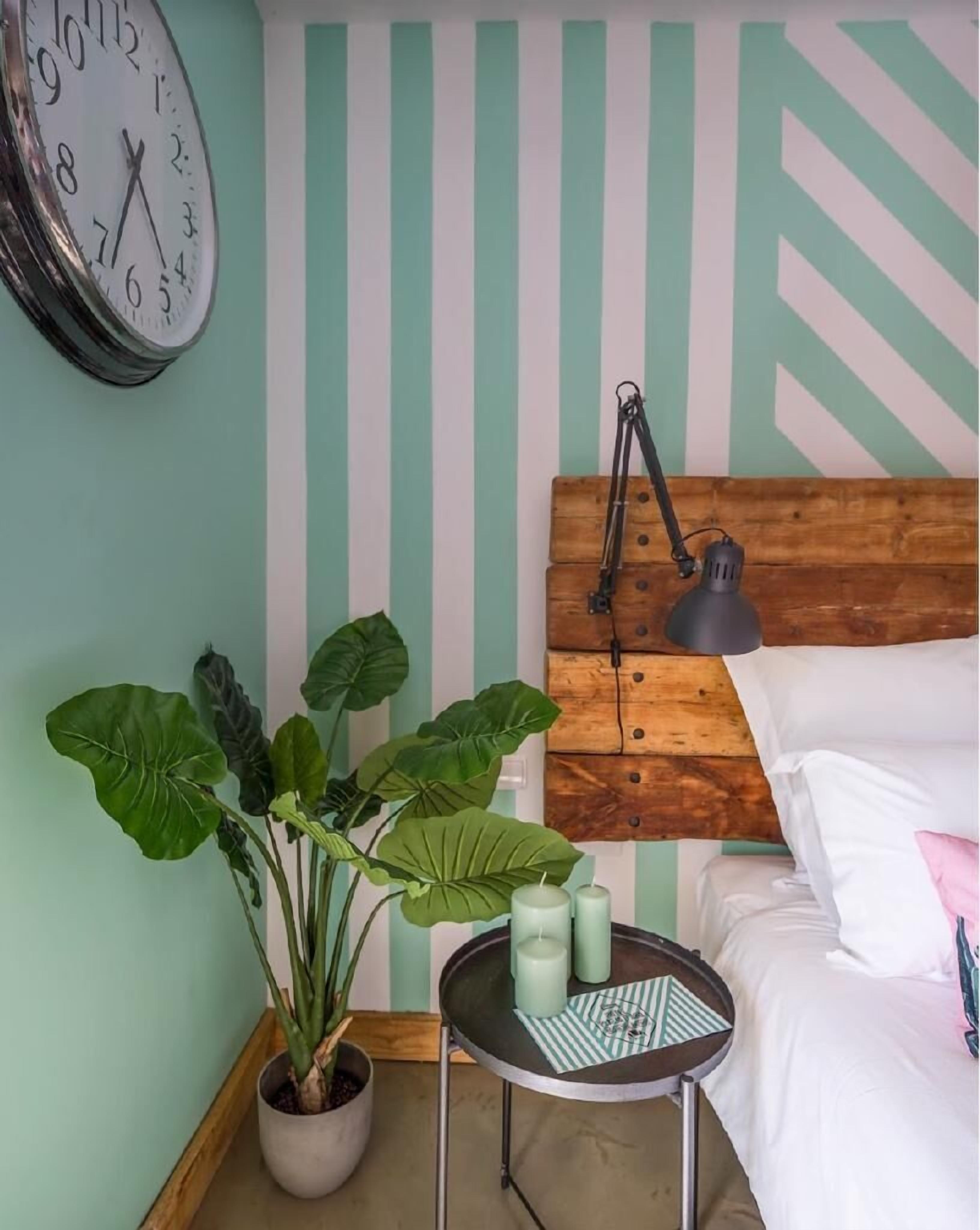 A bedroom with a bed, a bedside table with candles, a clock, and a potted plant.
