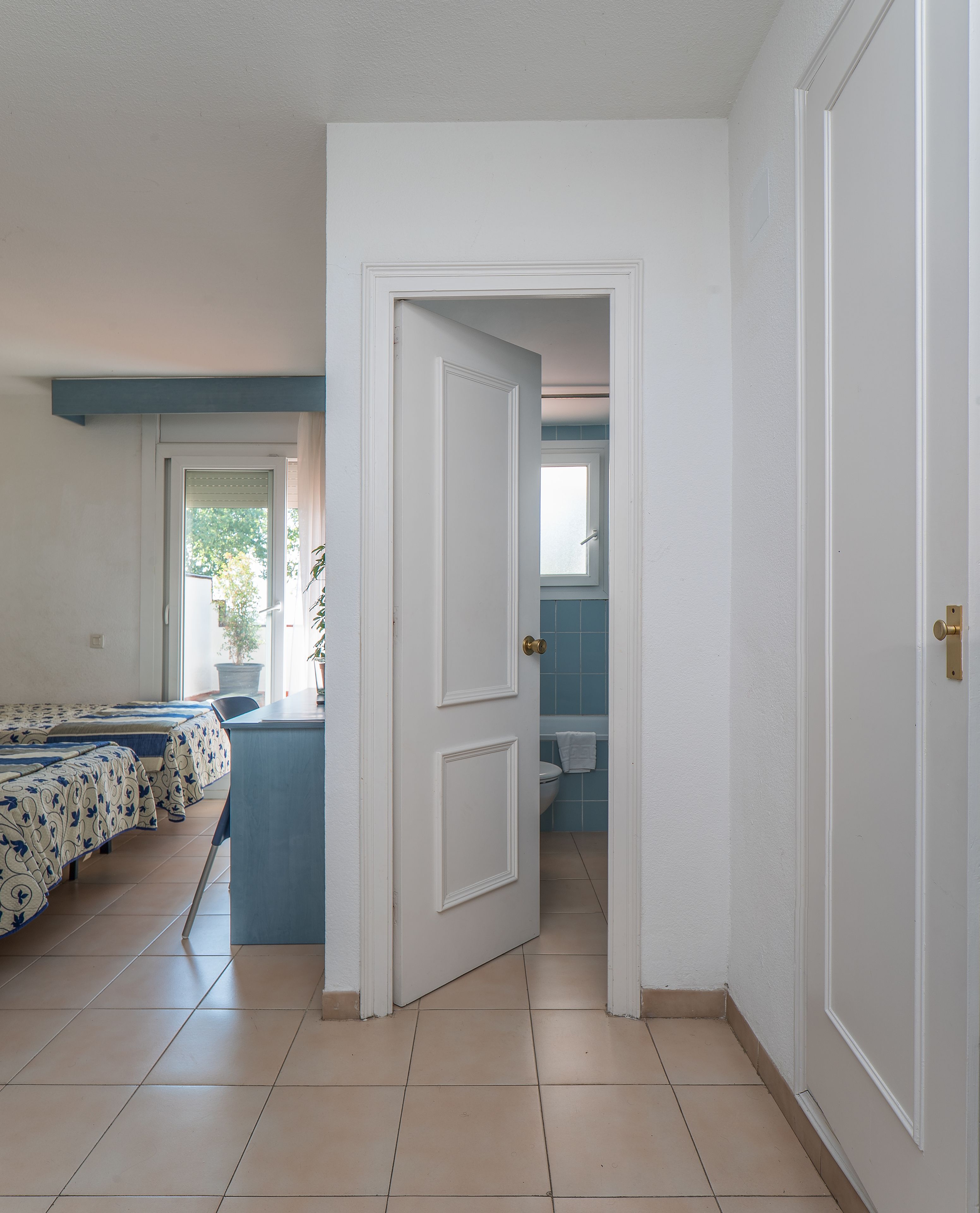A room with a bed, a desk, and a bathroom visible through an open door.