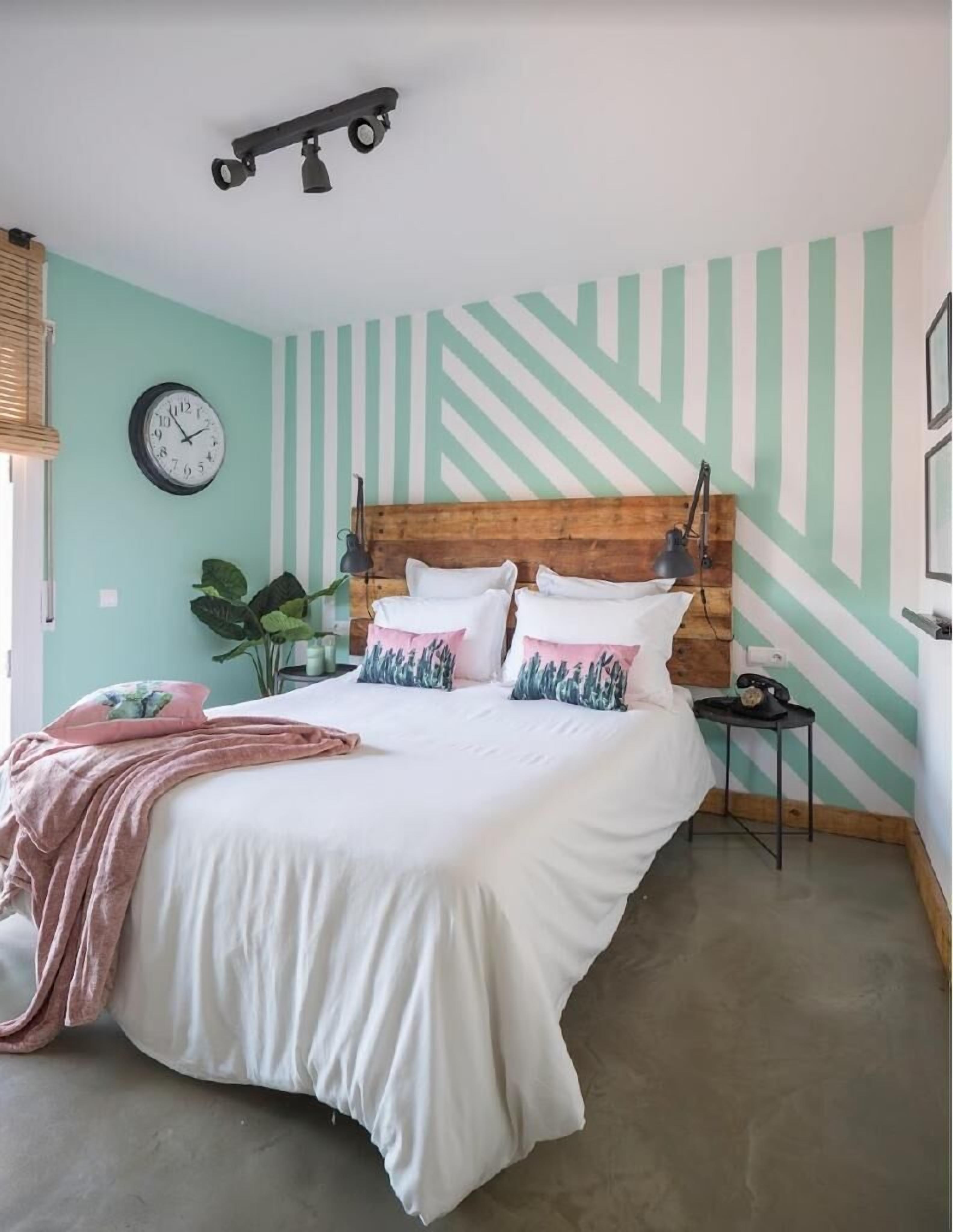 A bedroom with a bed, a clock, a plant, and a lamp.