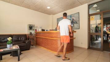 Un área de recepción con un sofá de cuero marrón, un mostrador de madera y una puerta de cristal que da al exterior.