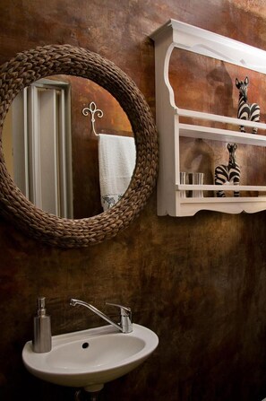 A bathroom with a round mirror, a white sink, and a shelf with decorative items. - a'Vue Guesthouse (Cape Town)