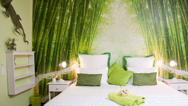 A bedroom with a bed, green pillows, a nightstand with a lamp, and a wall with a green curtain. - a'Vue Guesthouse (Cape Town)