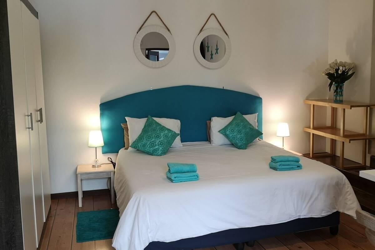 A neatly arranged bedroom with a bed, bedside lamps, a small table, and decorative mirrors on the wall.